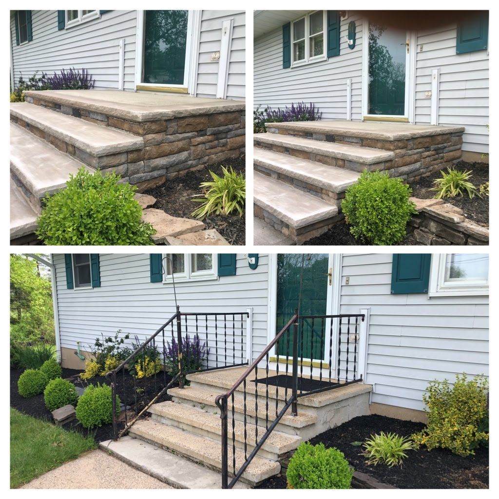Front porch steps with stone veneer and black railing beside a white house and landscaped shrubs