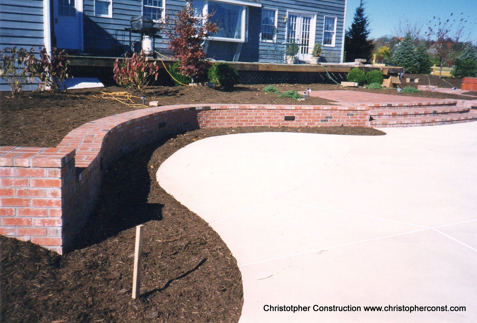 Curved brick retaining wall edging a concrete driveway in front of a blue house