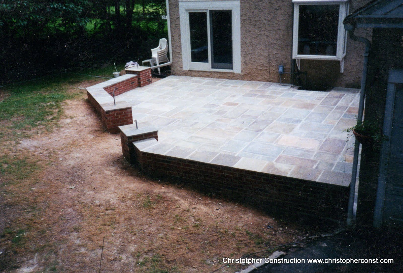 Brick patio with stone pavers, curved steps, and white French doors beside a house