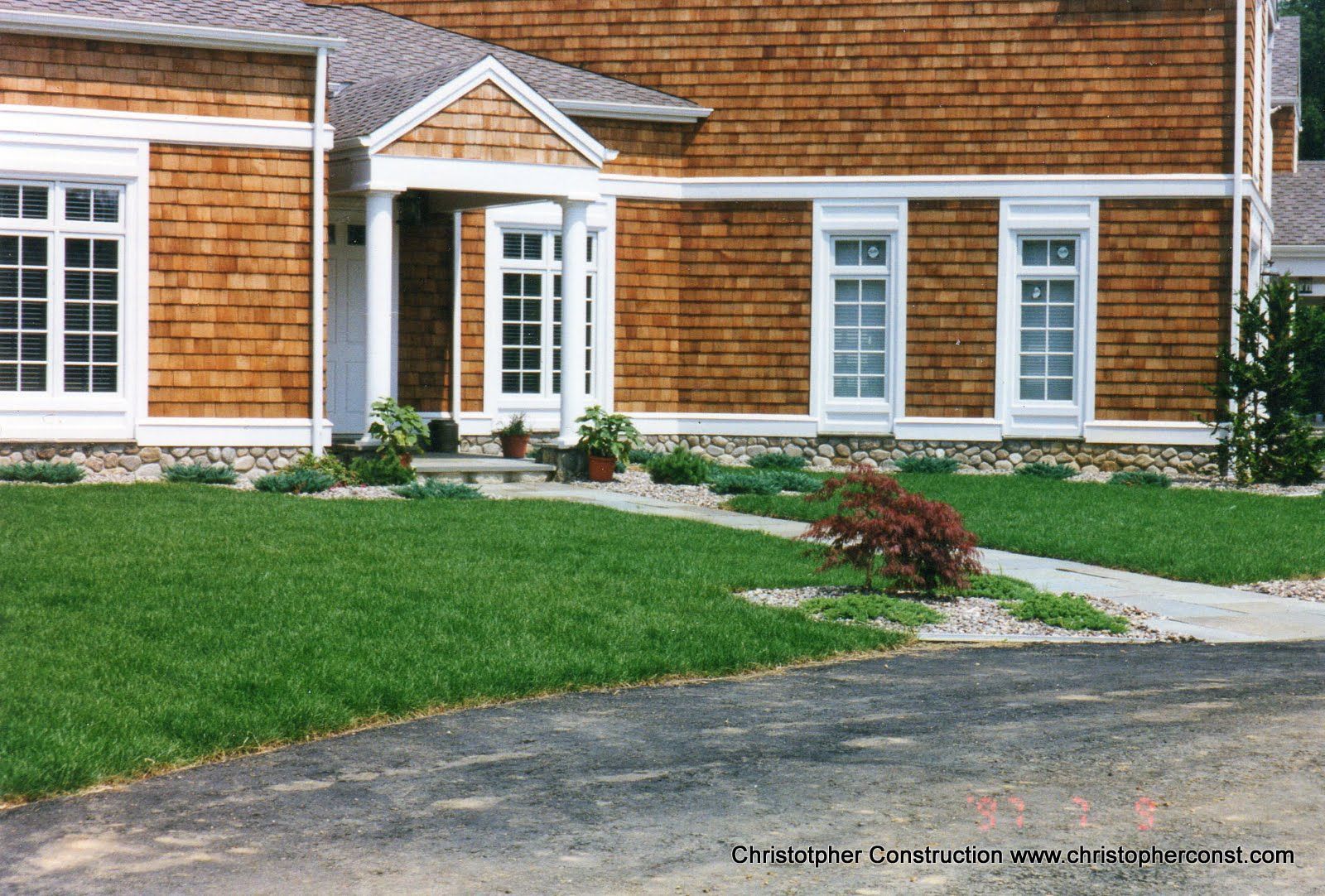 Suburban house with orange shingle siding, white trim, front lawn, and curved driveway