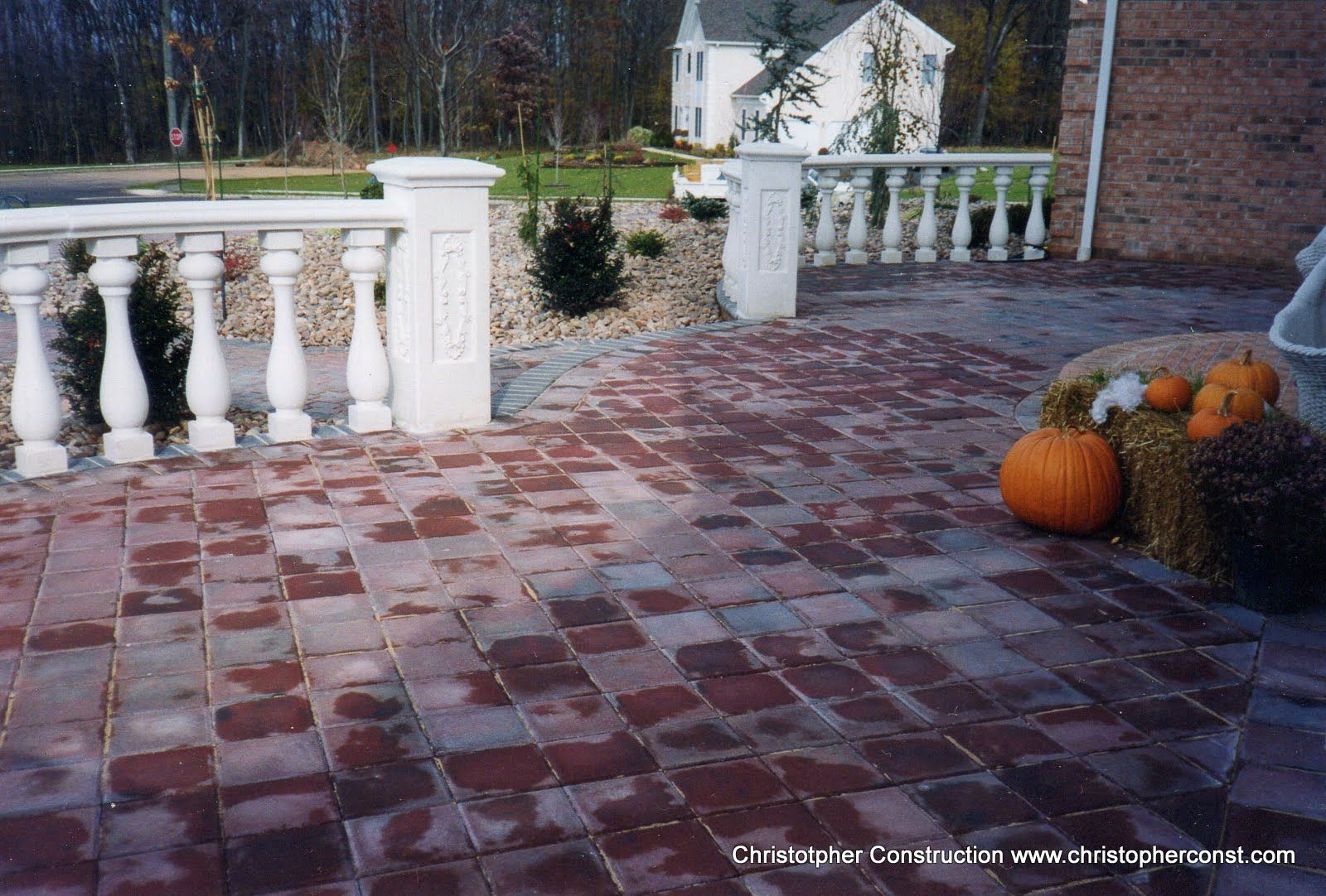 Brick patio with white balustrade, pumpkins, and autumn decor by a house porch
