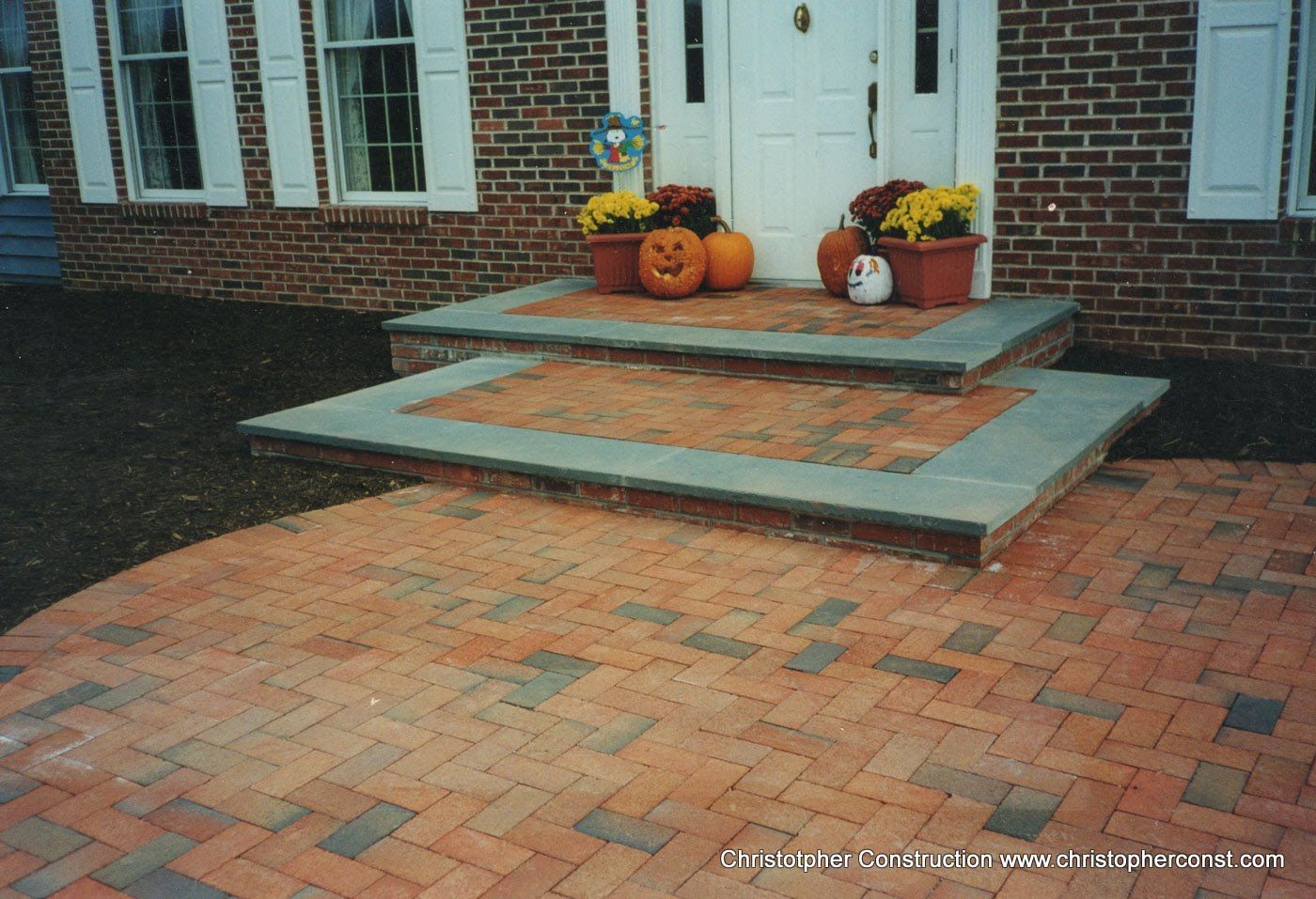 Front porch with brick steps, gray ramps, and fall pumpkins by white double doors