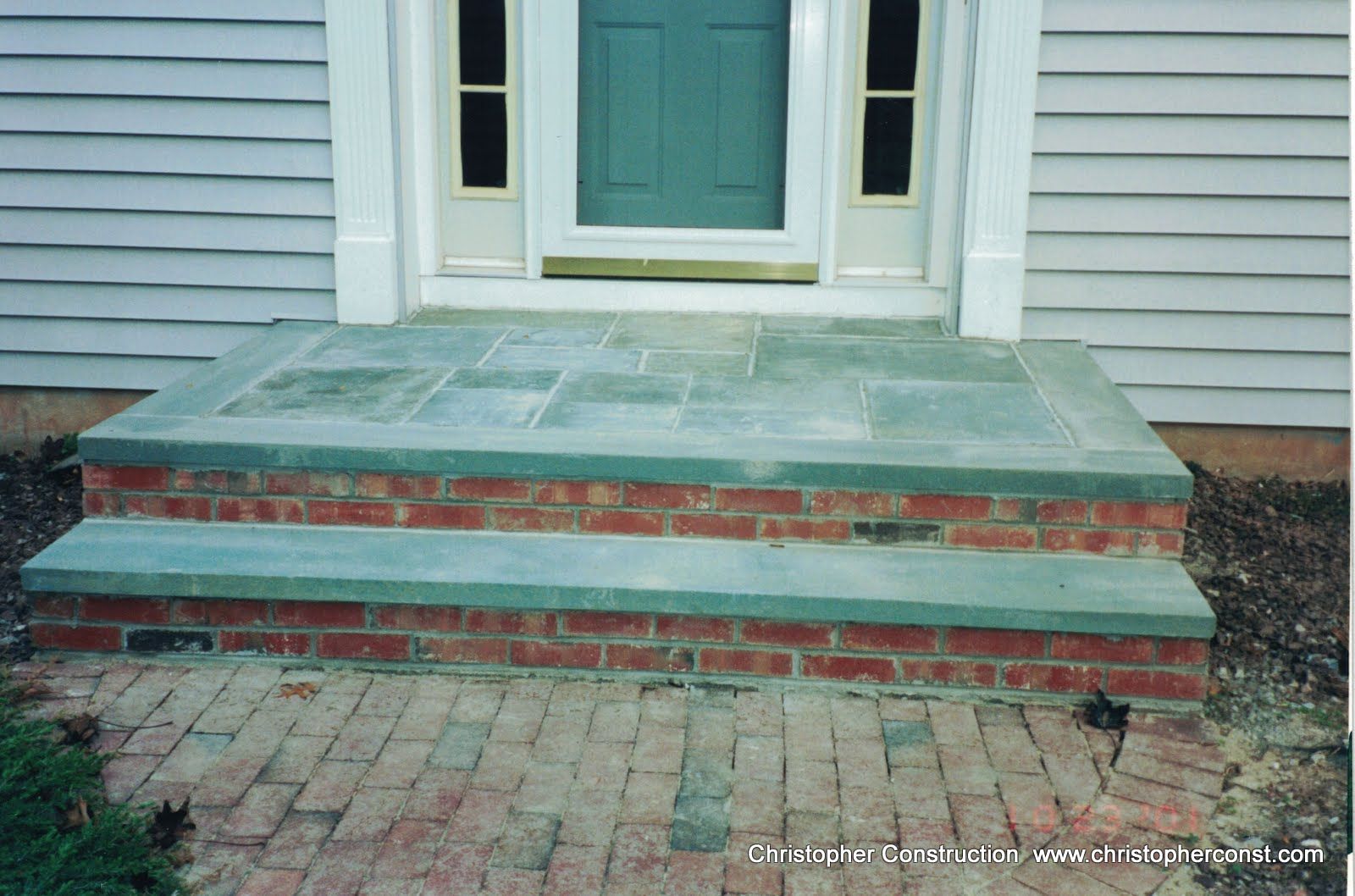 Brick front steps with a green stone landing leading to a white house door