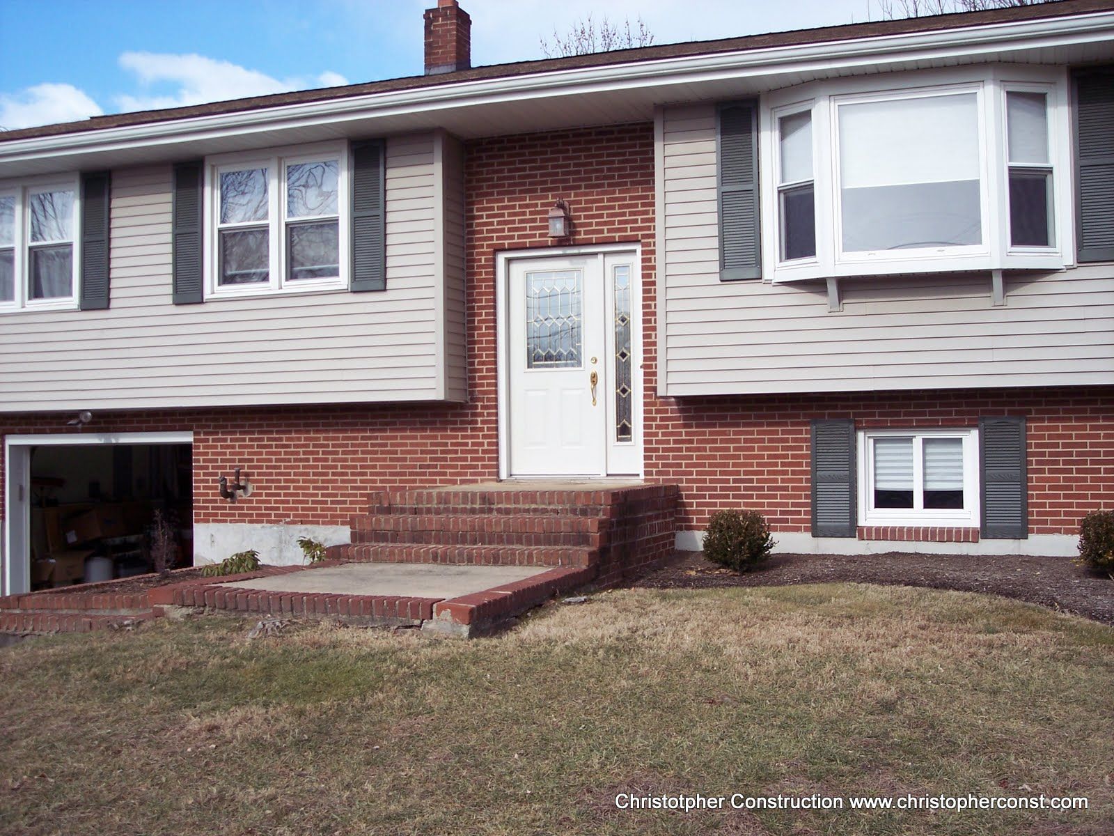 Front view of a brick suburban house with beige siding, white bay window, and a small front porch.