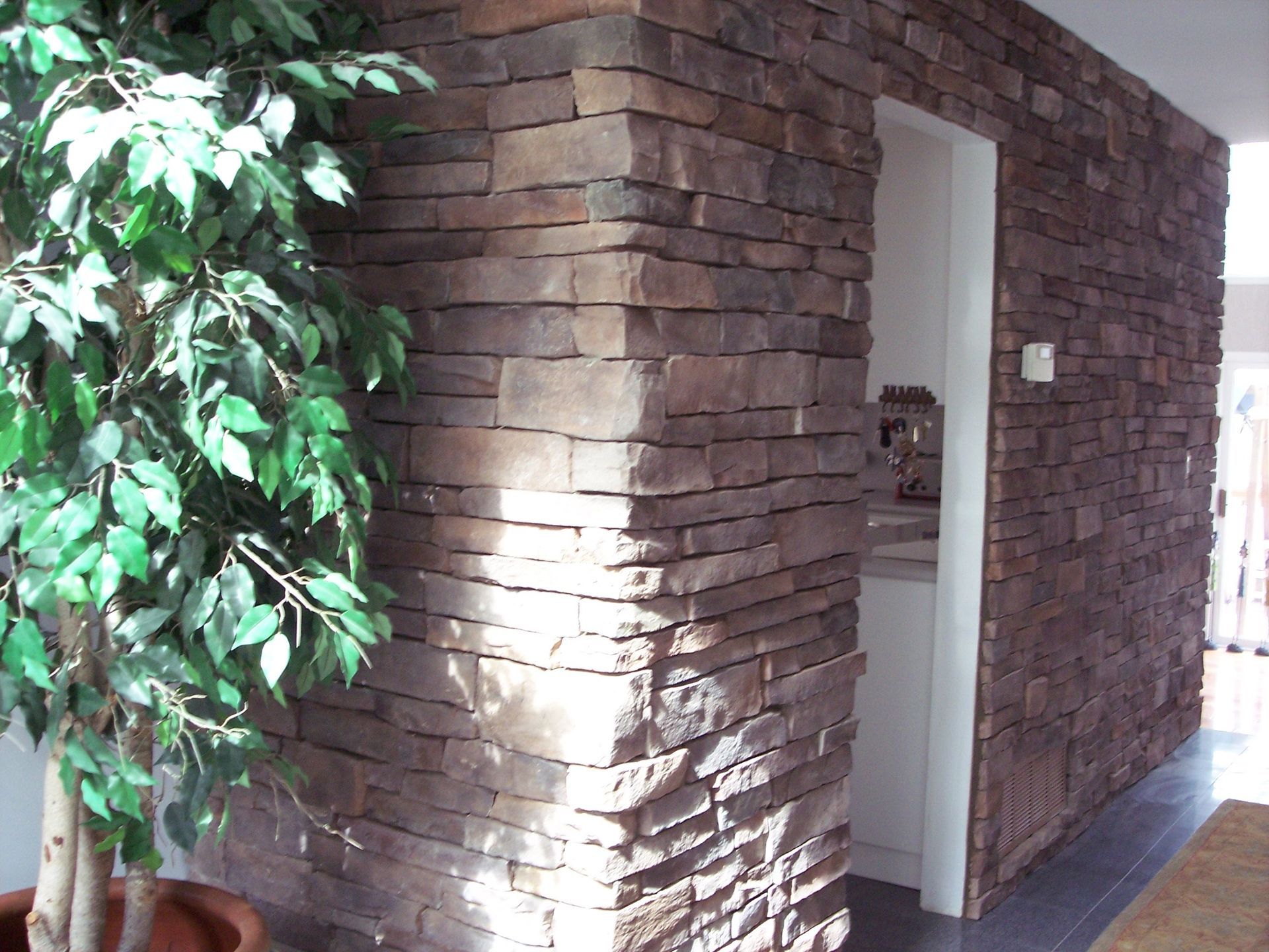 Brick building corner with a doorway beside a leafy tree in sunlight