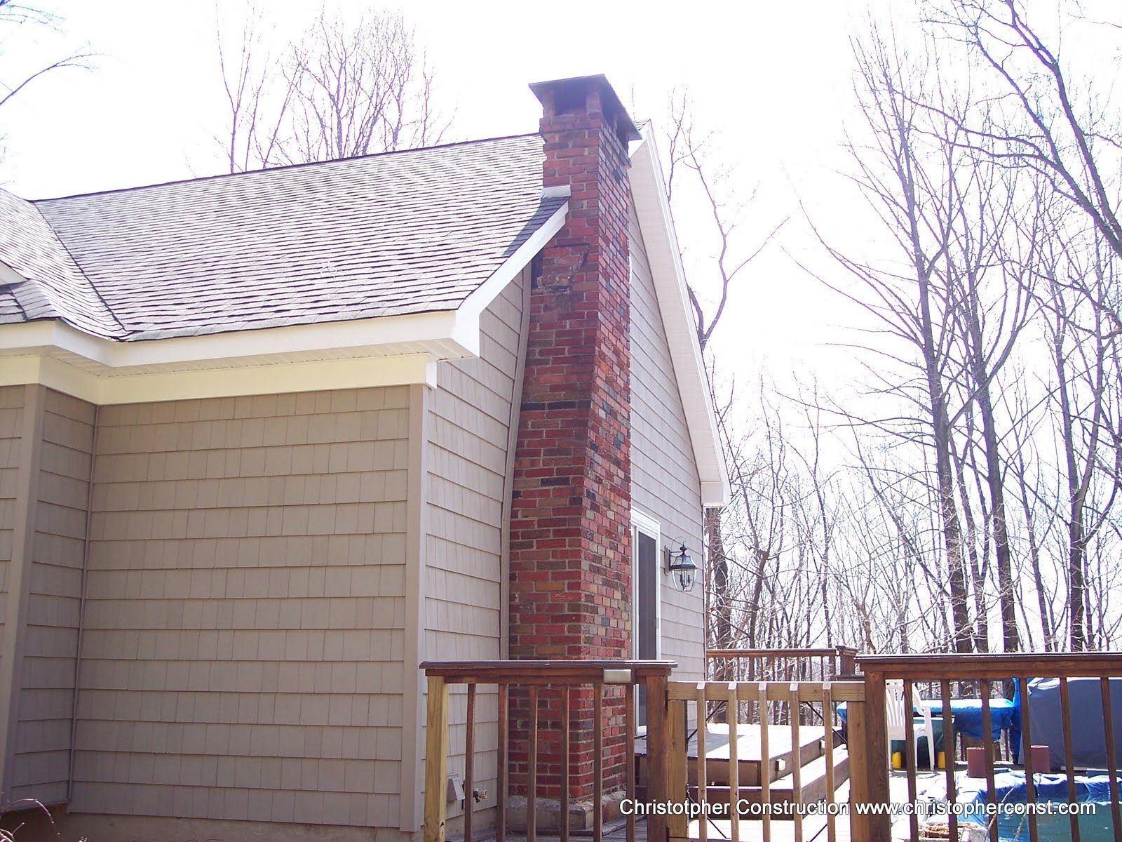 Snow-dusted house exterior with brick chimney and wooden fence in a leafless winter yard