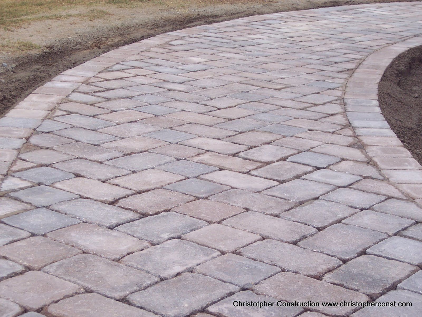 Curved stone-paver pathway beside a landscaped dirt edge, viewed from above