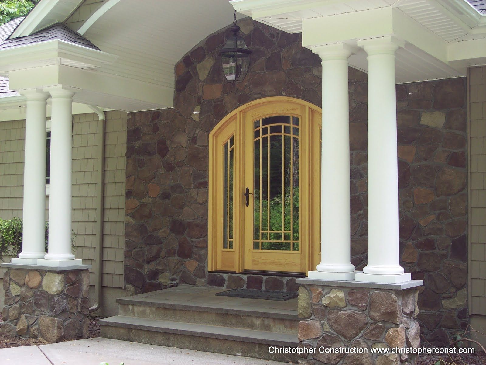 Stone-front house entry with a yellow arched door and white columns under a covered porch