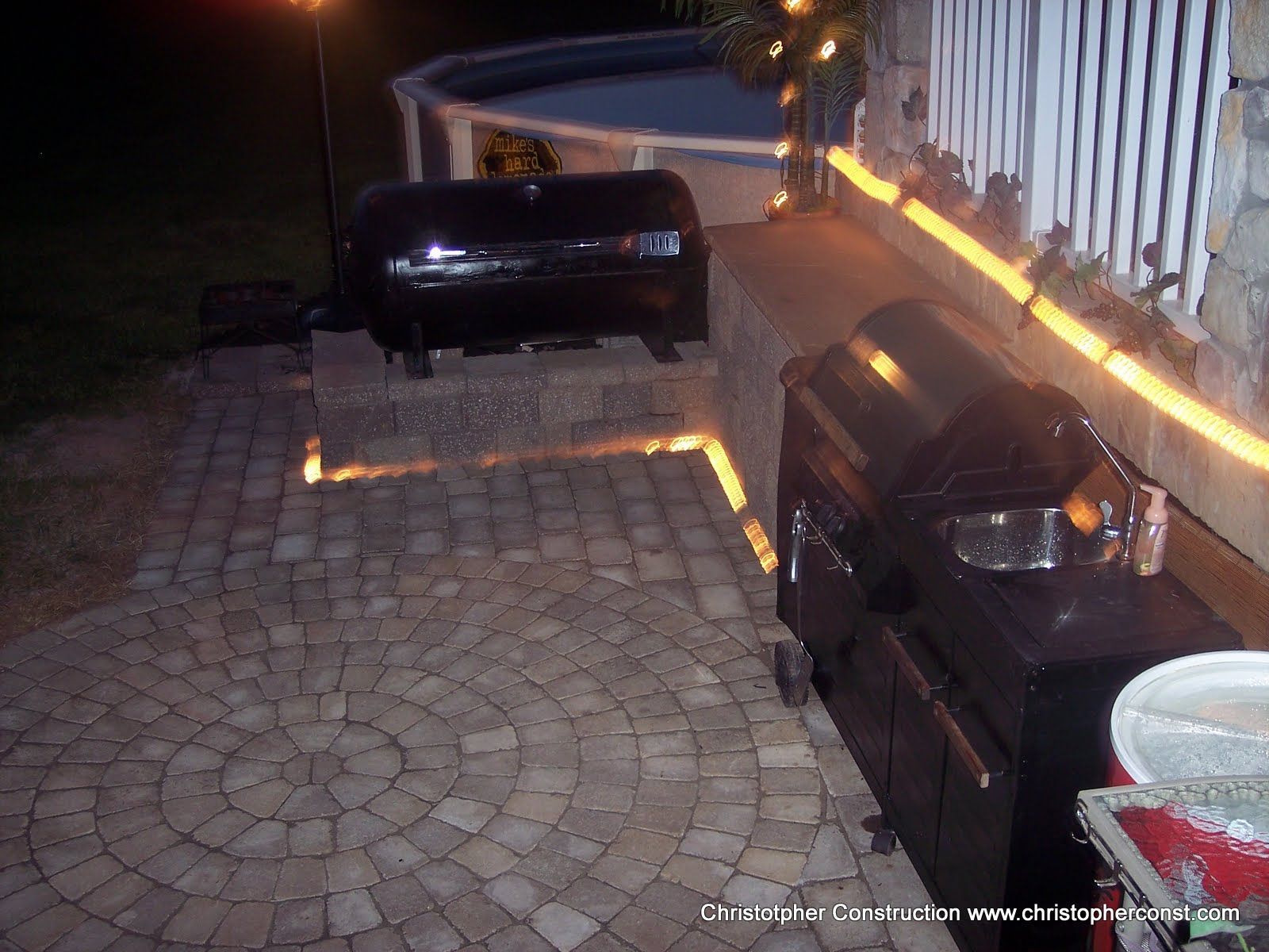 Two black cars parked on a stone driveway at night, lit by warm outdoor lights.