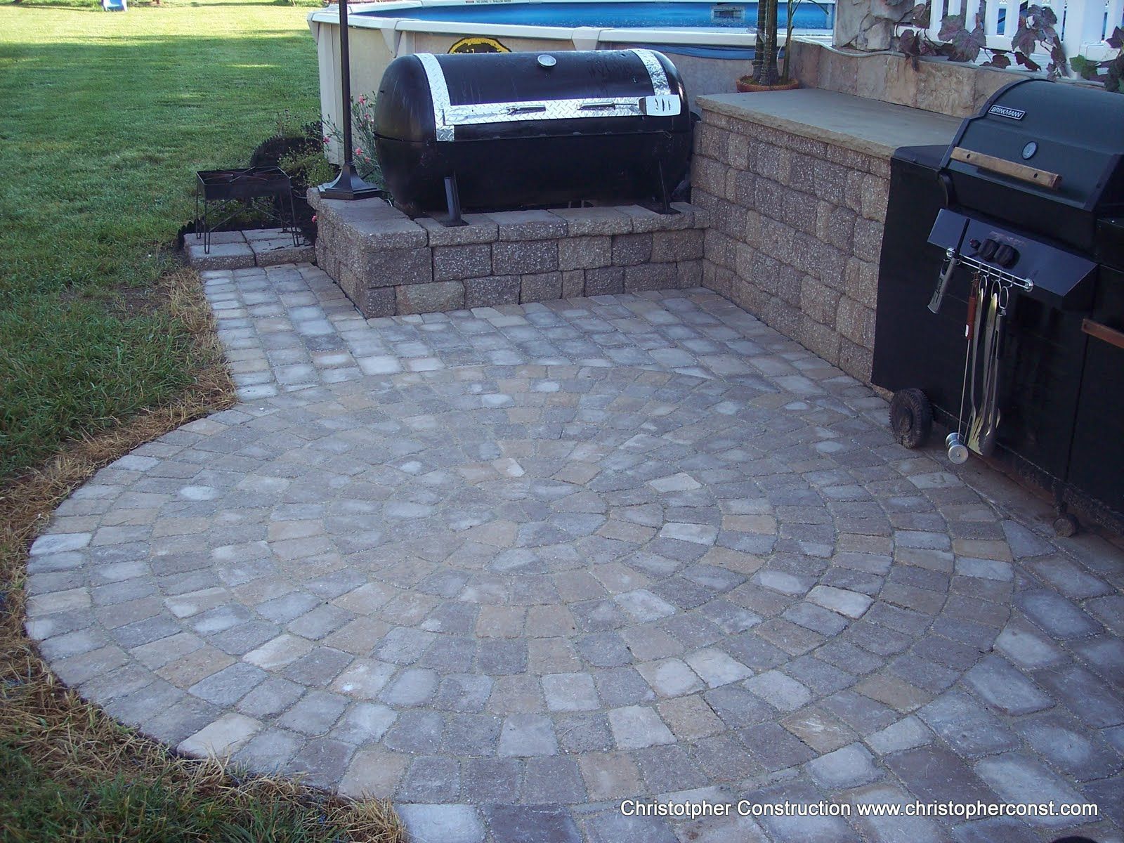 Stone patio with built-in black grill and raised planter beside a grassy yard