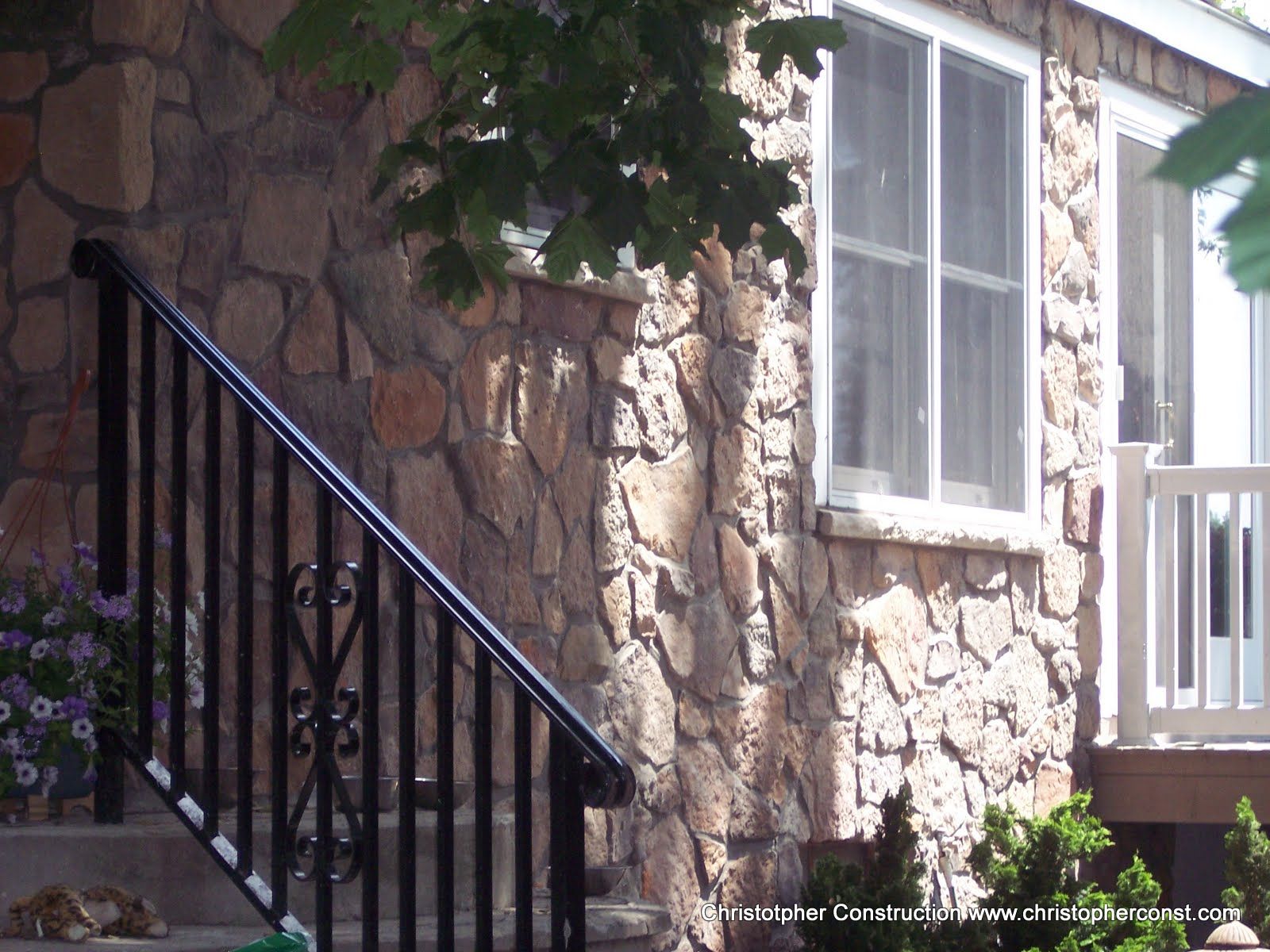 Stone house exterior with black metal stairs, white-framed windows, and green ivy overhead