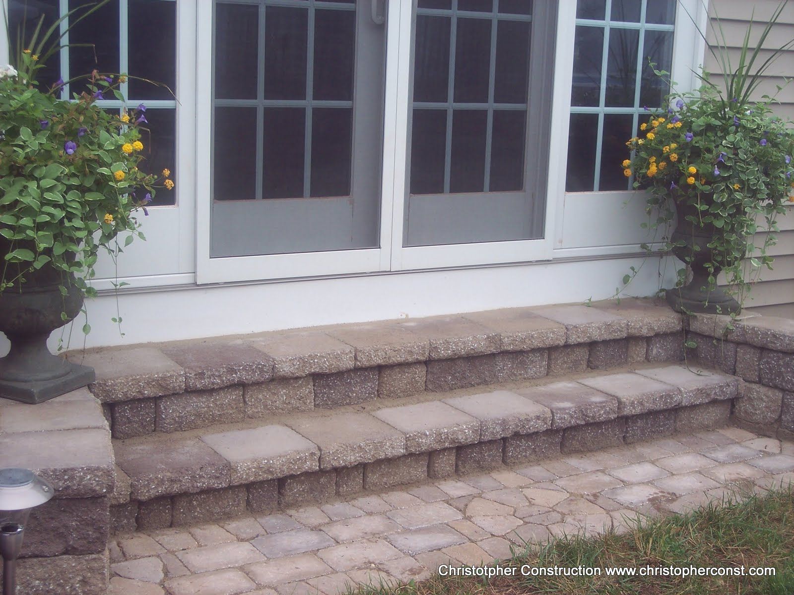 Stone steps leading to white French doors, flanked by hanging flower baskets and potted plants