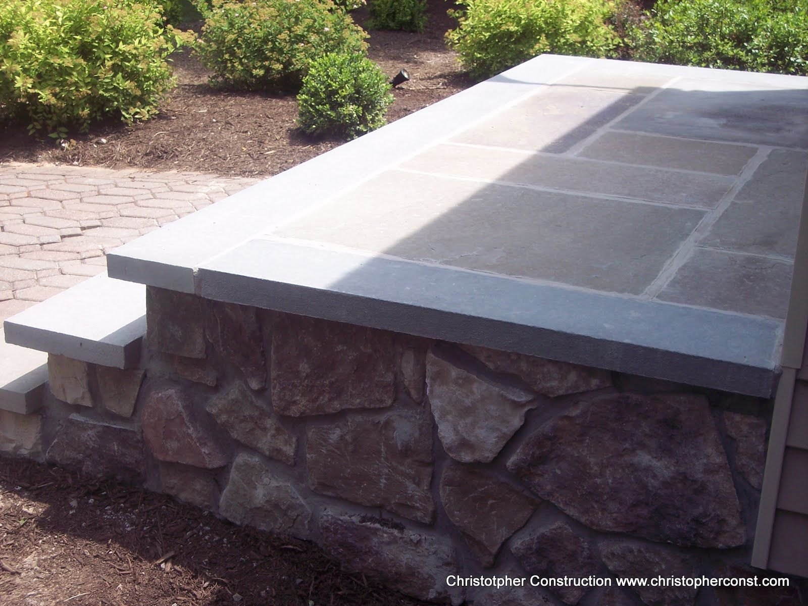 Stone outdoor bench with a light gray tiled top in a landscaped garden area