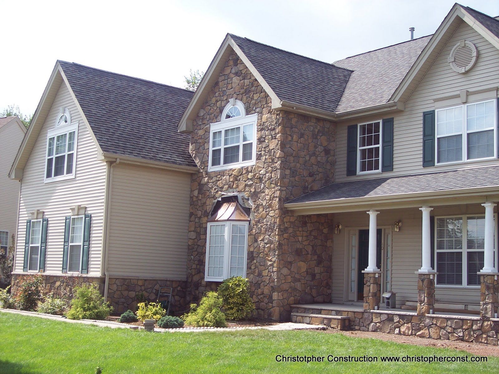 Two-story stone and siding suburban house with a front porch, shutters, and well-kept lawn