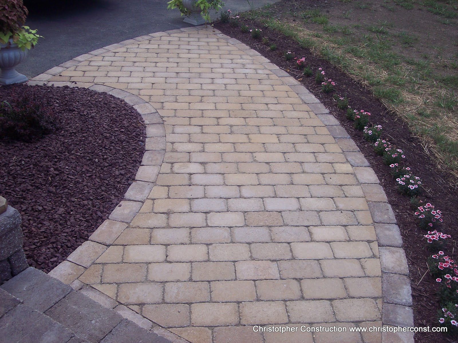 Curved stone walkway bordered by grass and flower beds in a landscaped garden