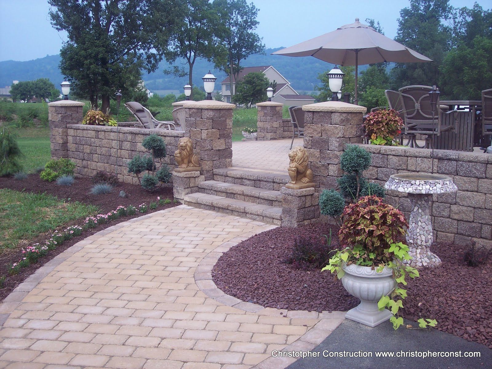 Stone pathway leading to a landscaped patio with steps, planters, and patio umbrella in a garden setting