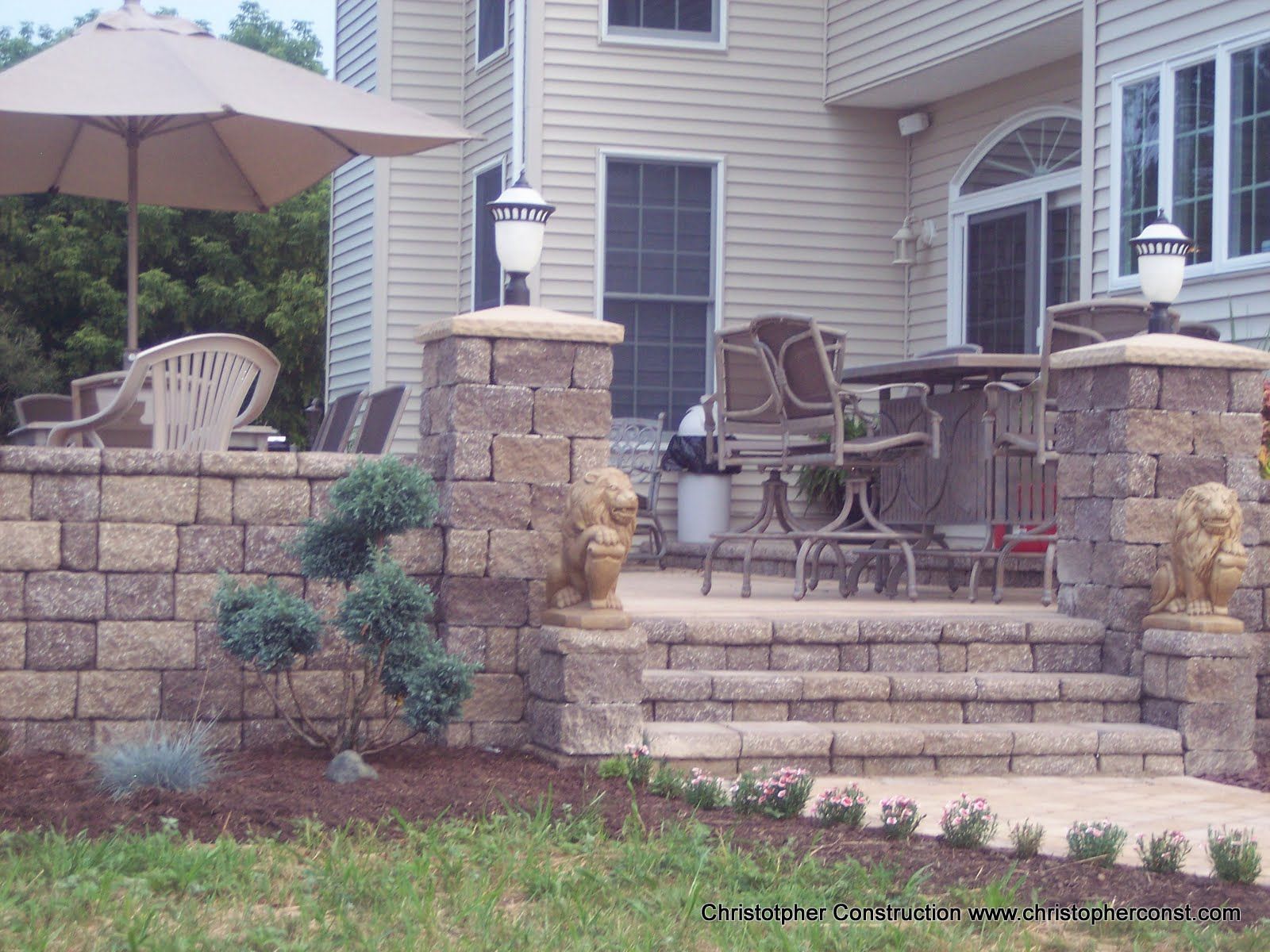 Stone patio with steps, umbrella, and outdoor seating beside a house entryway