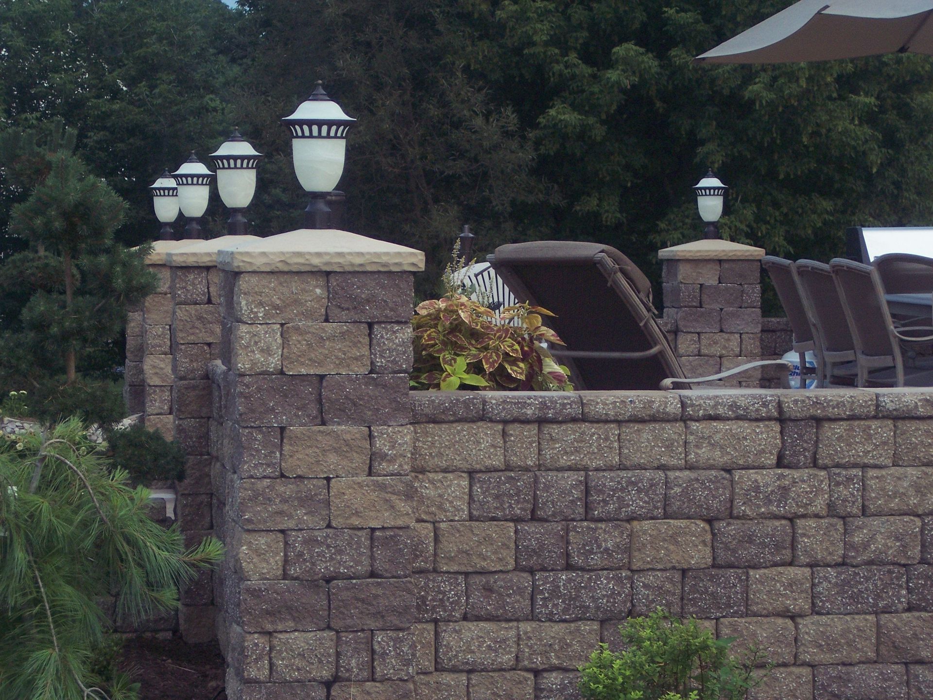 Stone patio wall with decorative lamps and lounge chairs beside a pool