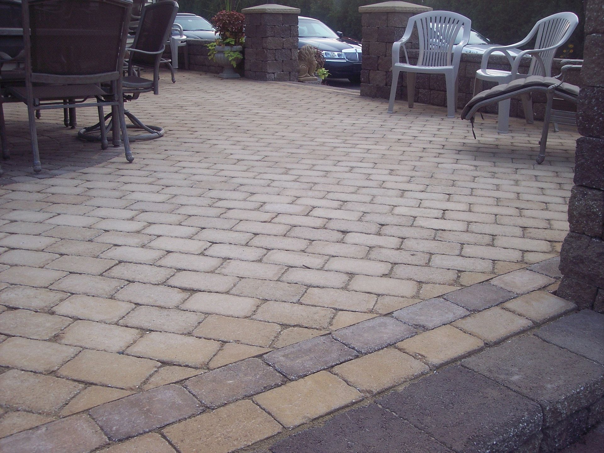 Stone patio with outdoor chairs and a table, leading to a parked car in the background