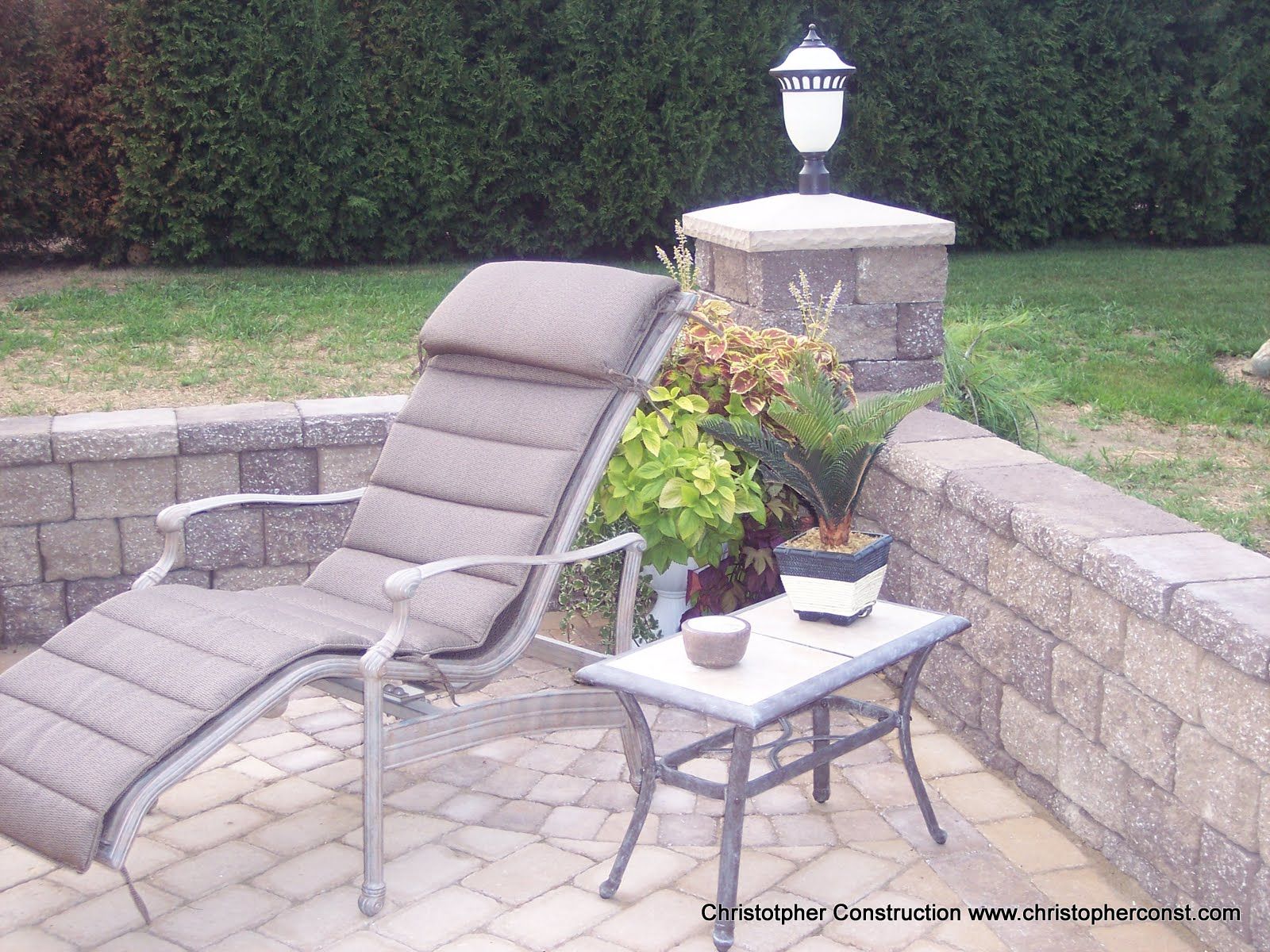Patio lounge chair beside a small table with potted flowers on a stone terrace.