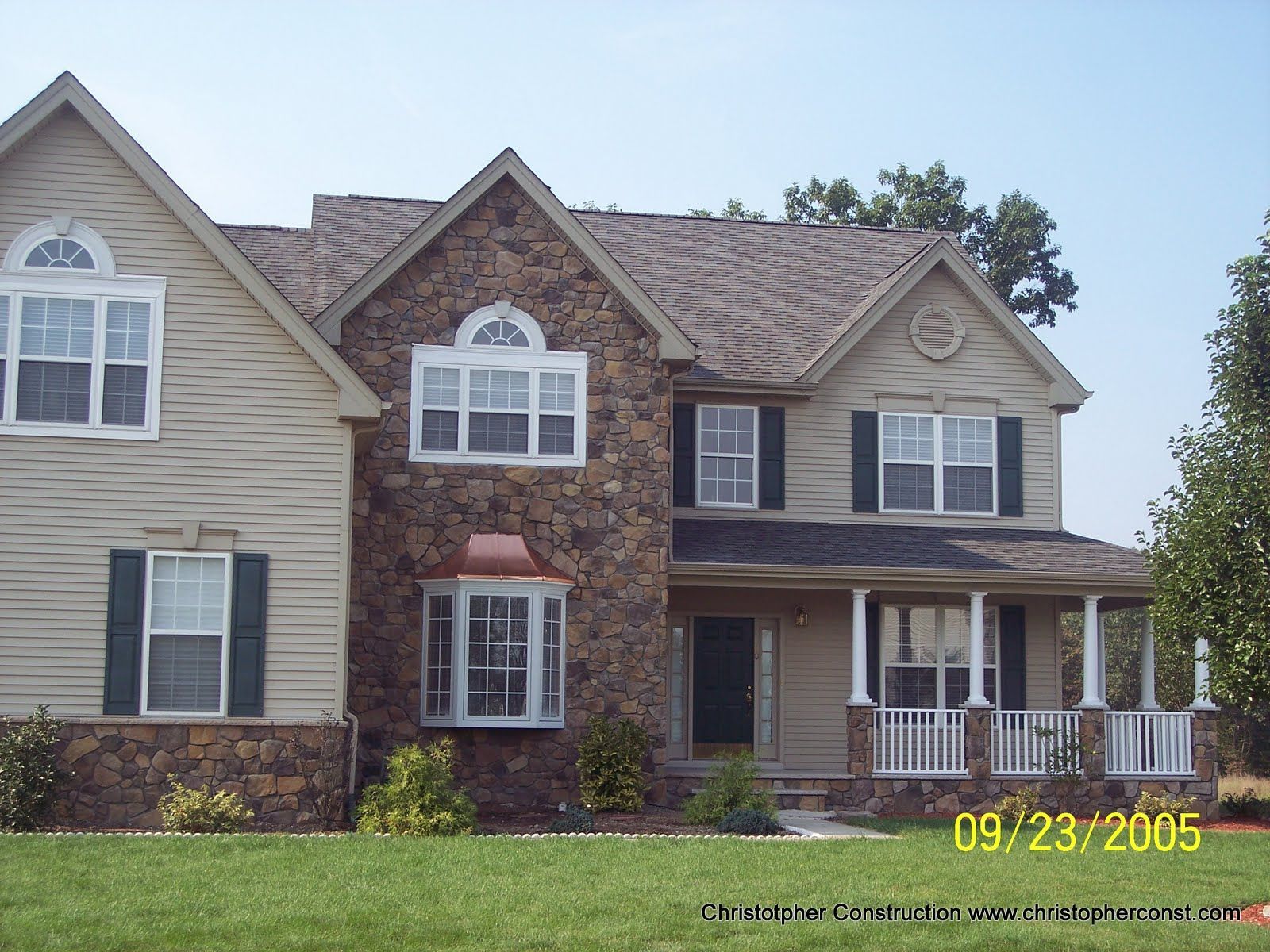 Two-story suburban house with tan siding, brick accents, and a front porch, dated 09-23-2005