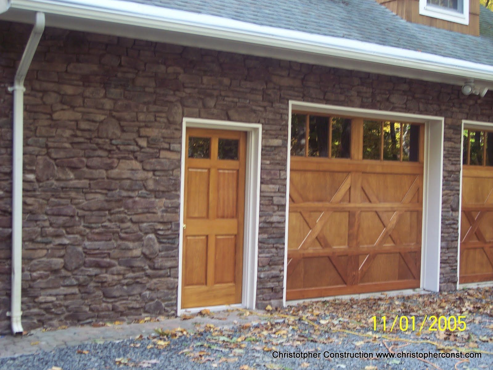 Stone-faced garage with wood doors and a side entry door on a house exterior