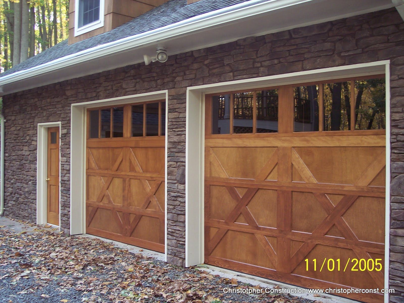 Brick house with two wooden garage doors and a side entry door covered in fallen leaves