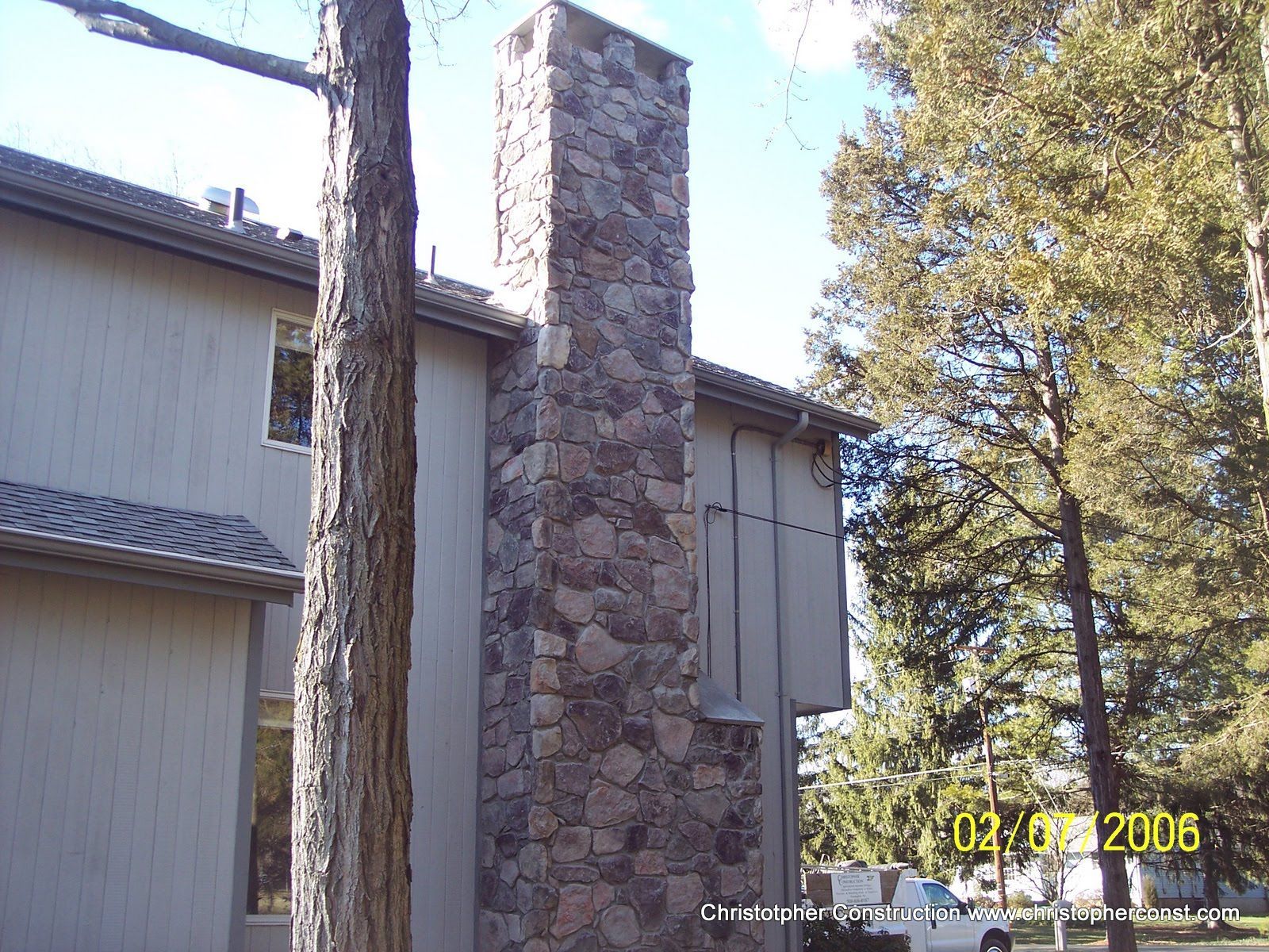 Stone chimney on a beige apartment building beside a tall tree in daylight