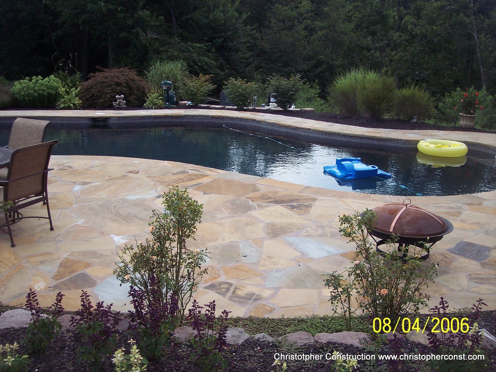 Backyard pool with stone patio, lounge chair, and colorful float toys at dusk