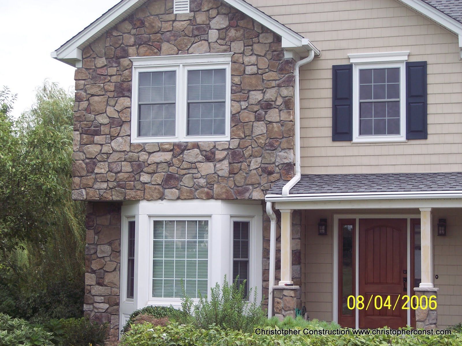 Two-story stone and beige house with white-trim windows and a red front door