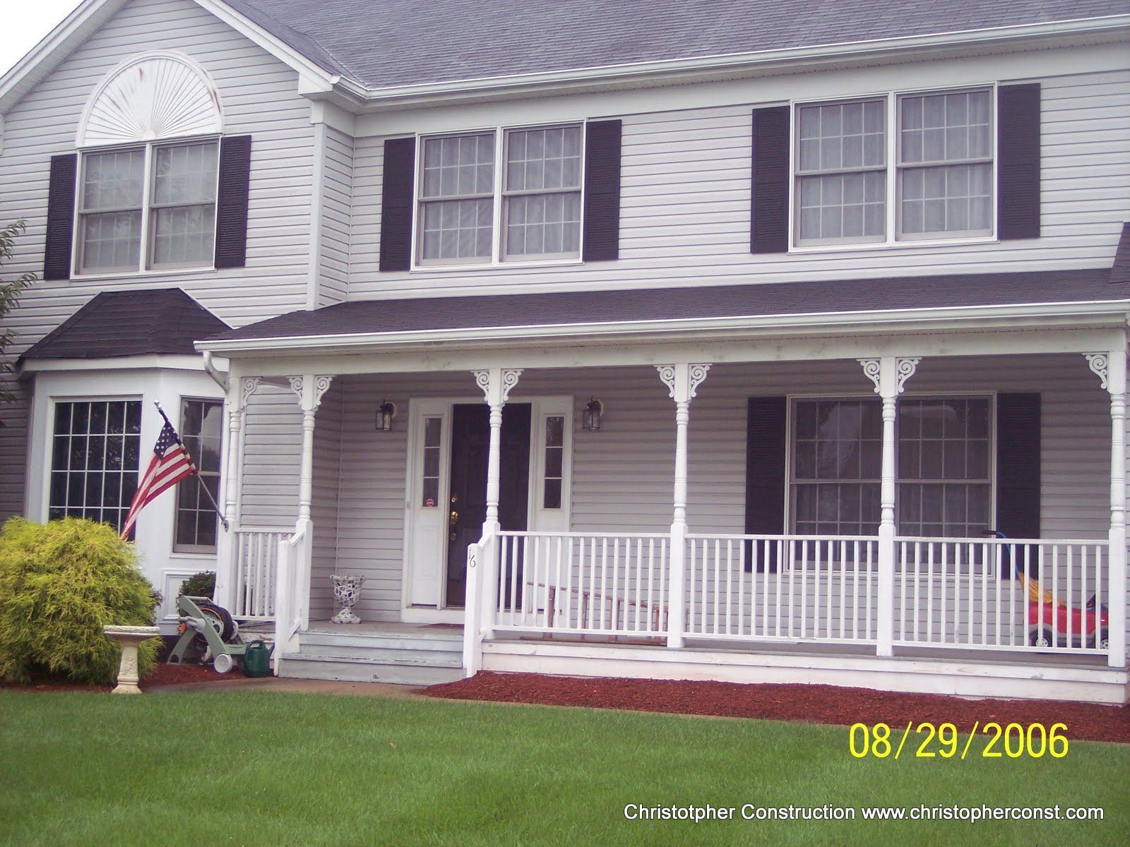 Suburban house with white porch, American flag, and green lawn under overcast sky.