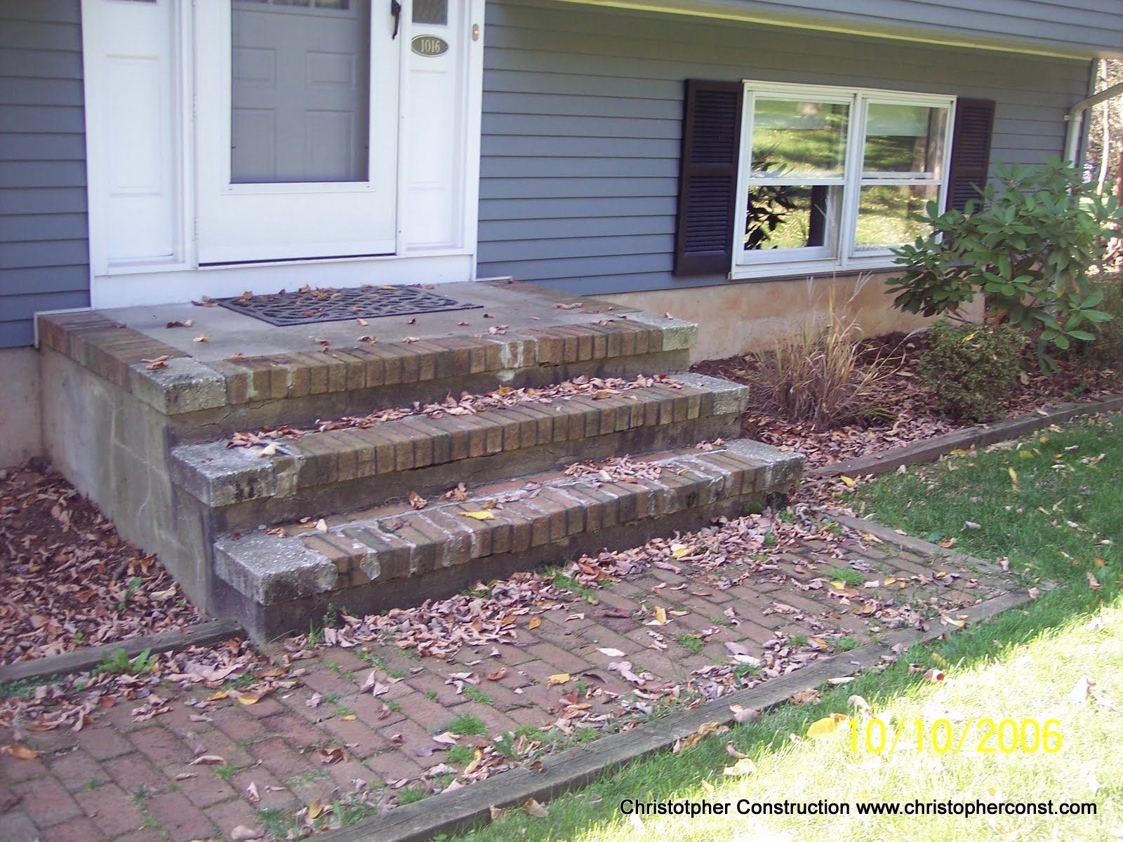 Front steps of a house with uneven brick paving and a short concrete landing by the door.