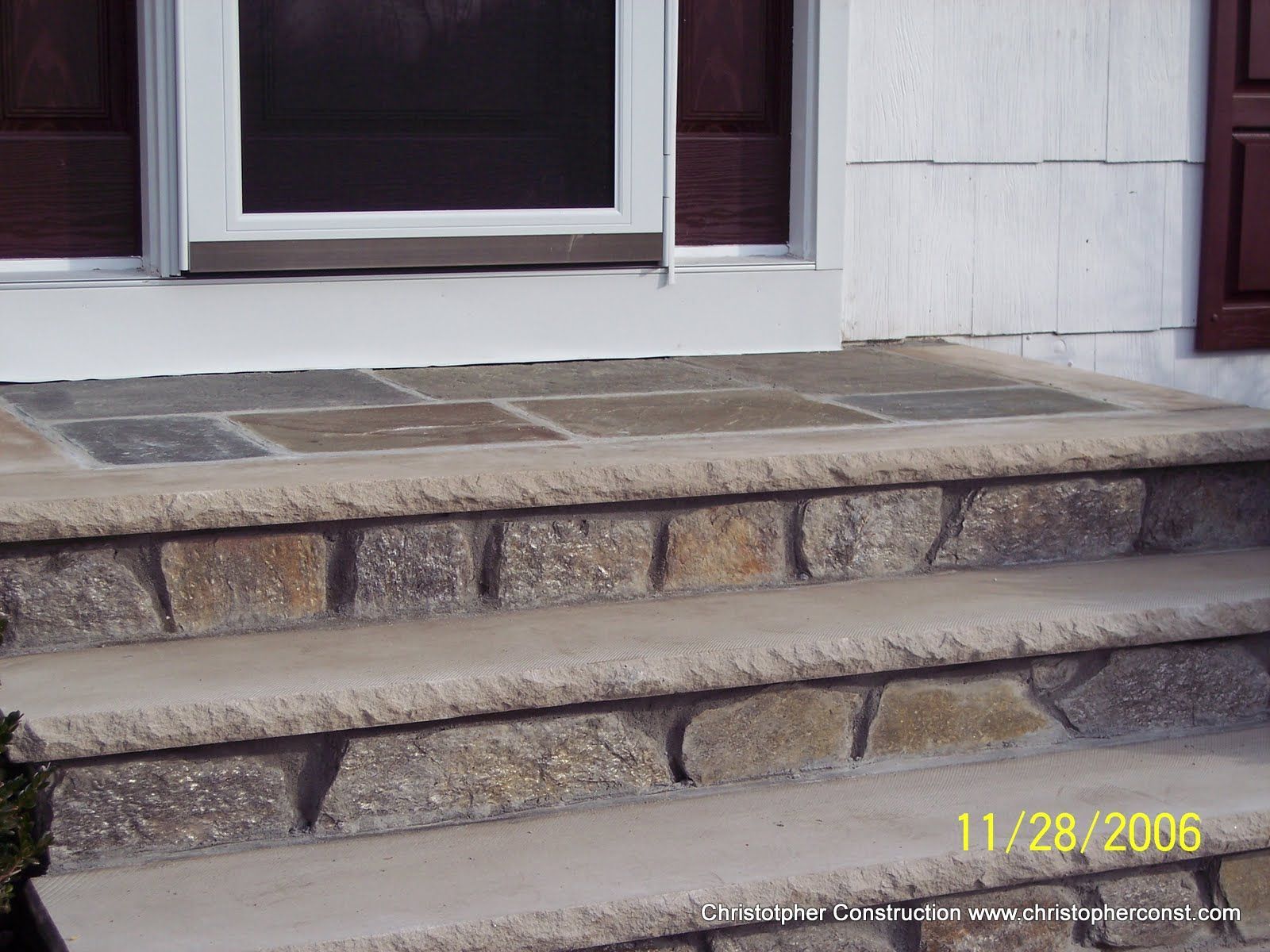 Stone front steps leading to a white house porch with window and dark shutters