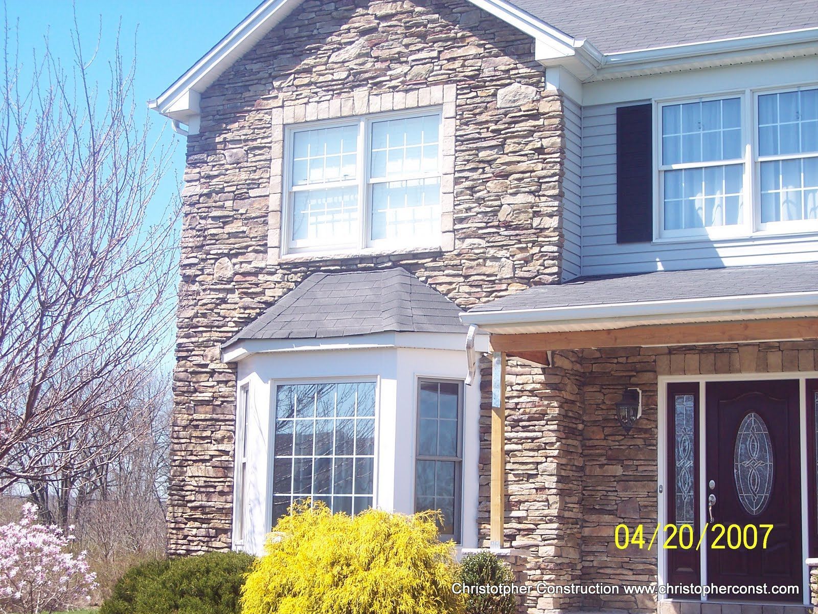 Two-story stone house with white trim and a front porch under a clear blue sky
