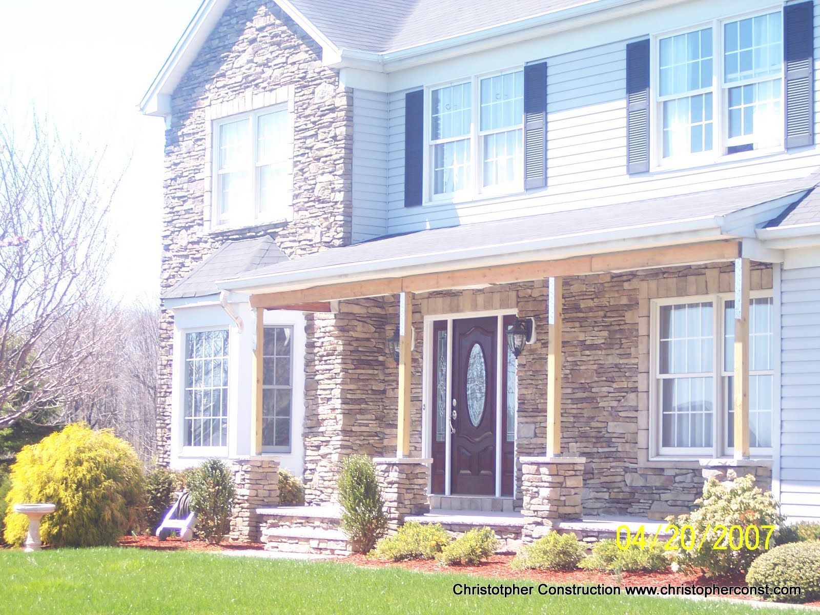 Two-story brick house with white trim, front porch, and dormer windows on a sunny day