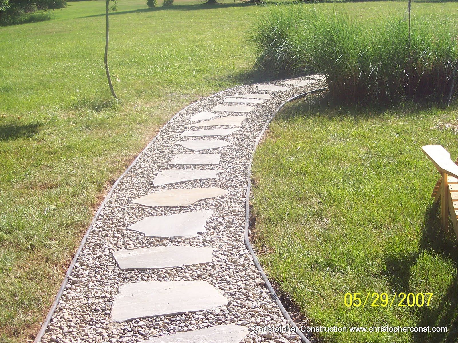 Curved stone stepping-stone path through green grass, leading toward a shrub in a sunny yard.