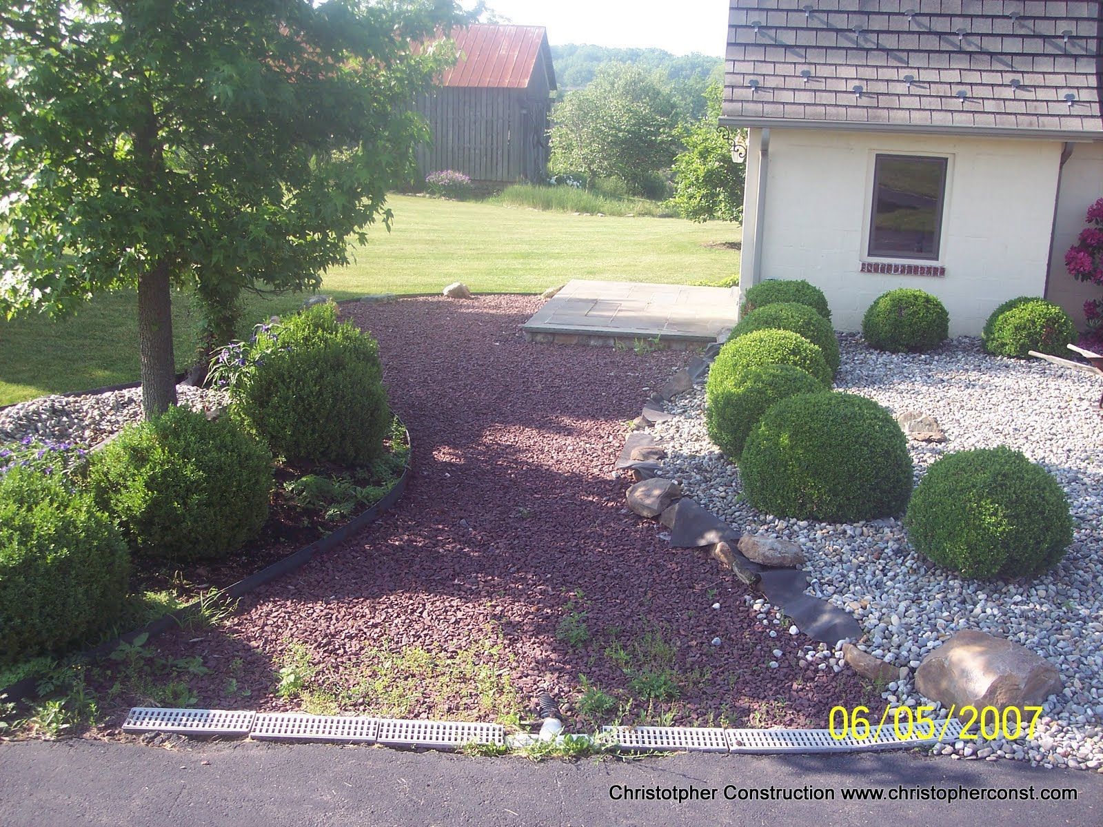 Front yard with manicured shrubs, gravel path, and house exterior in daylight