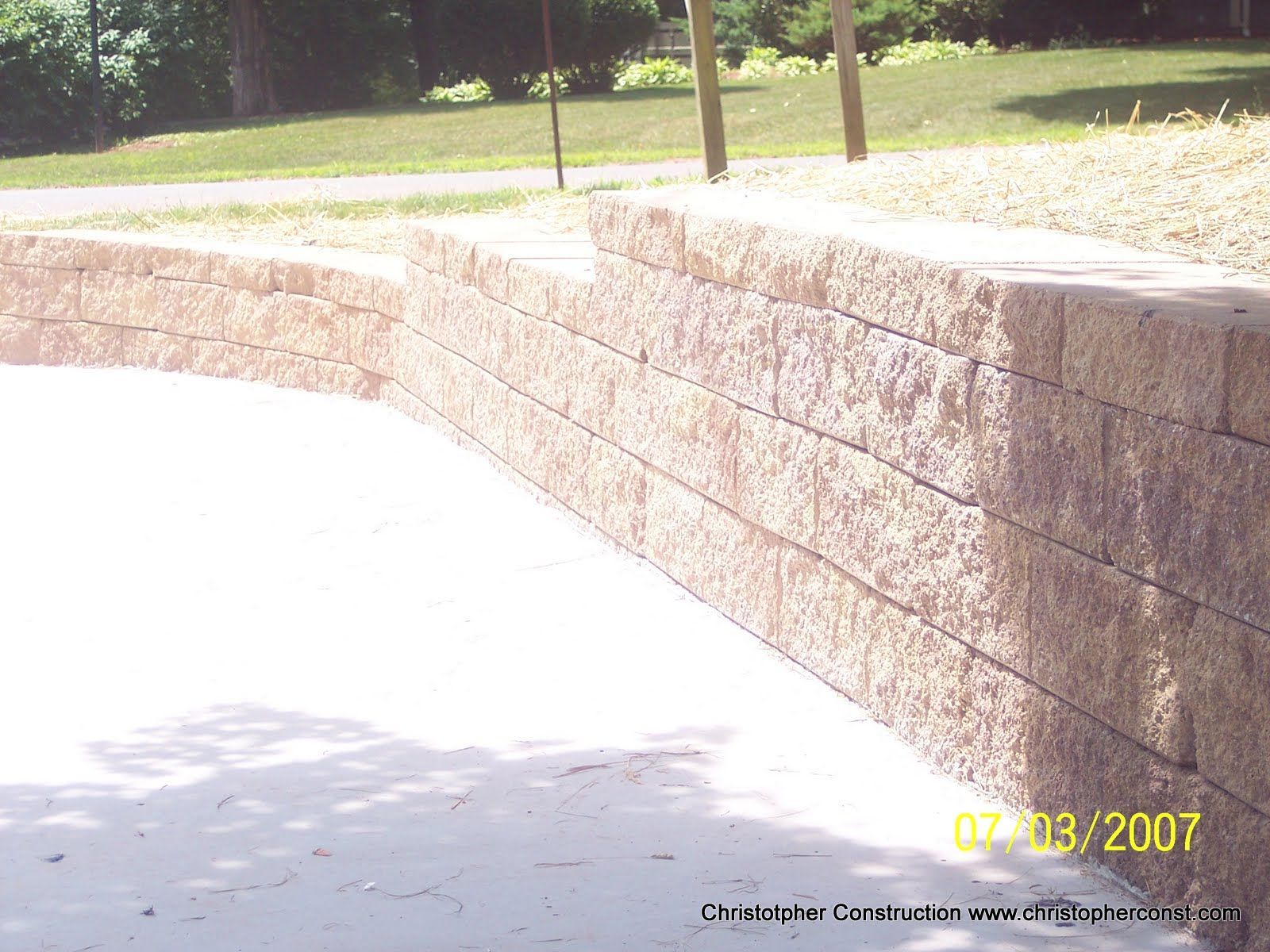 Curved tan brick retaining wall beside a bright concrete path in a sunny park