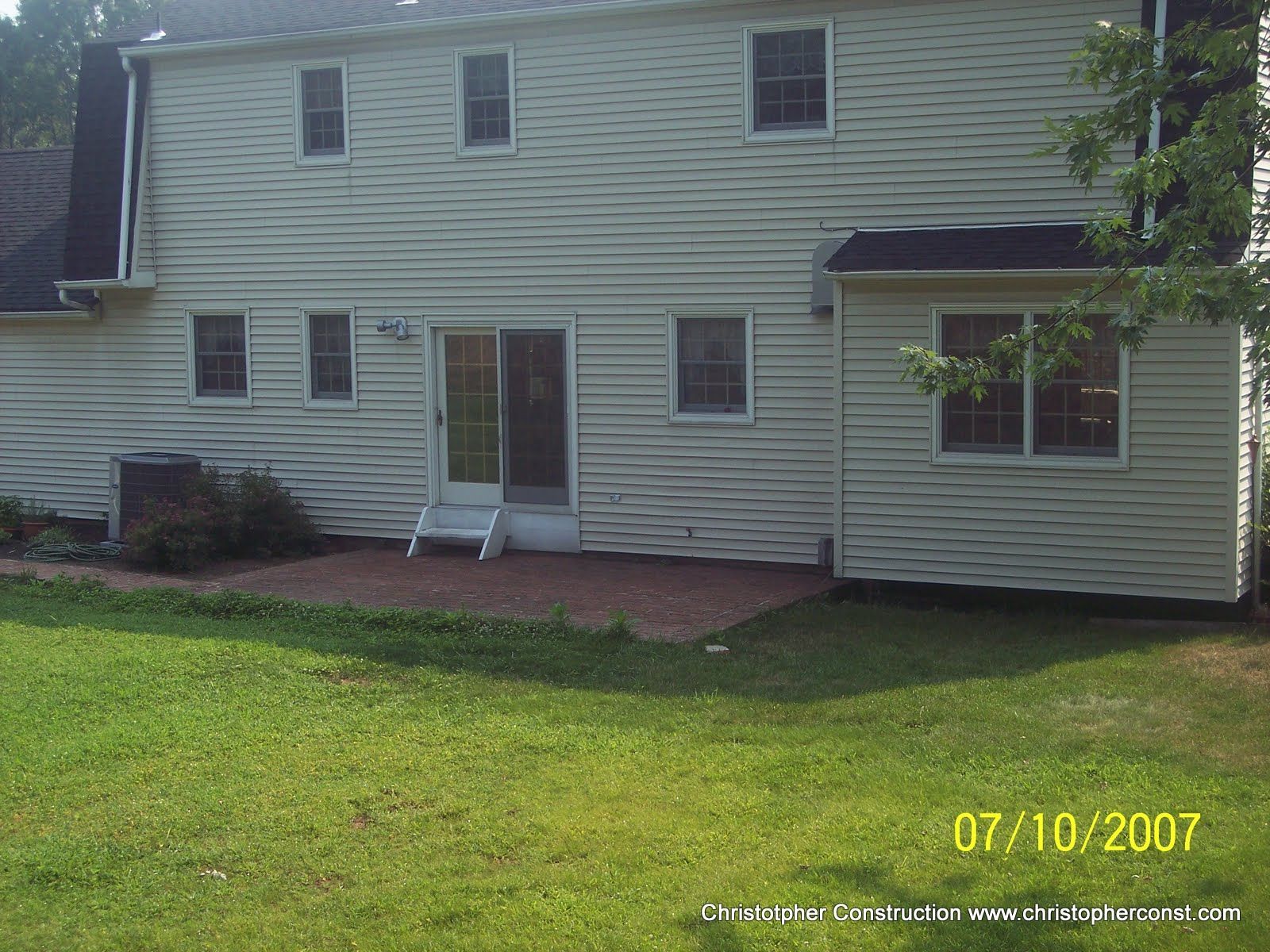 White two-story house with a small porch, brick patio, and green lawn.
