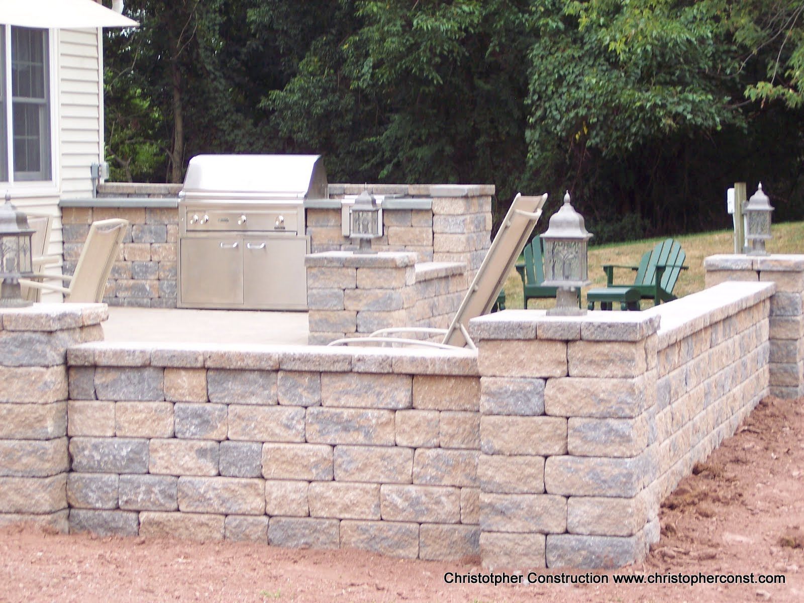 Stone outdoor kitchen and fire pit area with built-in grill and seating wall in a backyard