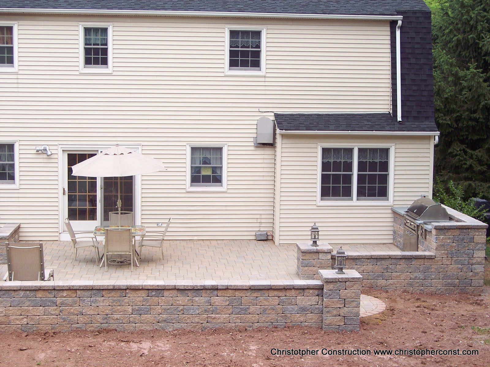 Backyard patio with outdoor table and chairs beside a beige two-story house