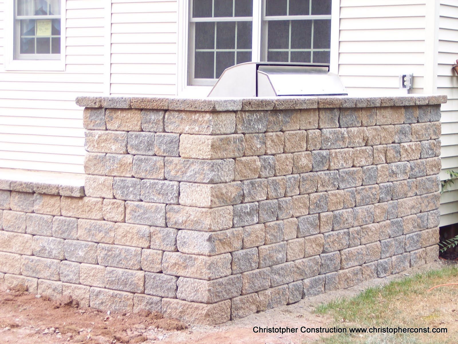 Stone retaining wall beside a white house, with a metal railing on top.