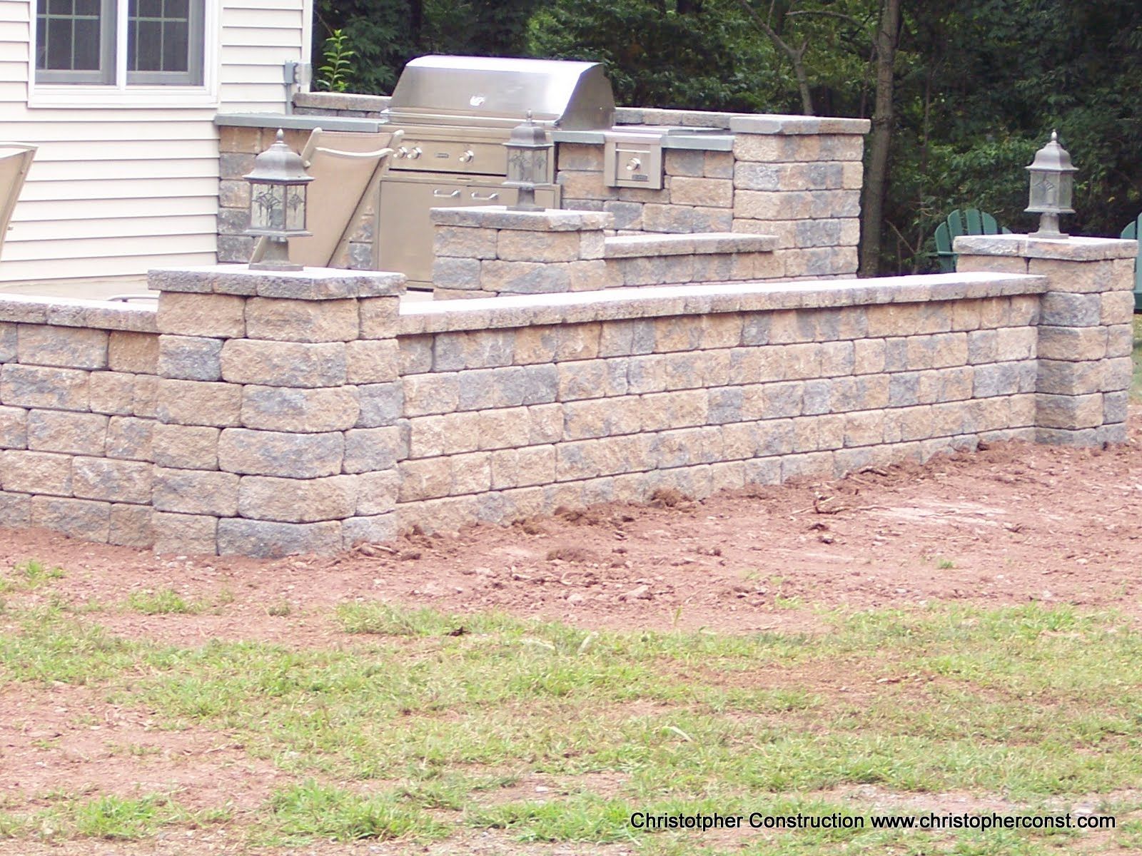 Stone patio retaining wall and outdoor fire pit beside a house lawn