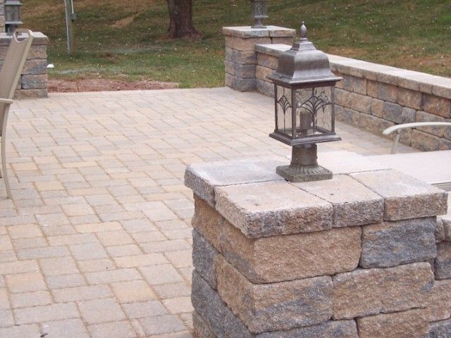 Stone patio with decorative lantern on a low stone wall in a landscaped outdoor area