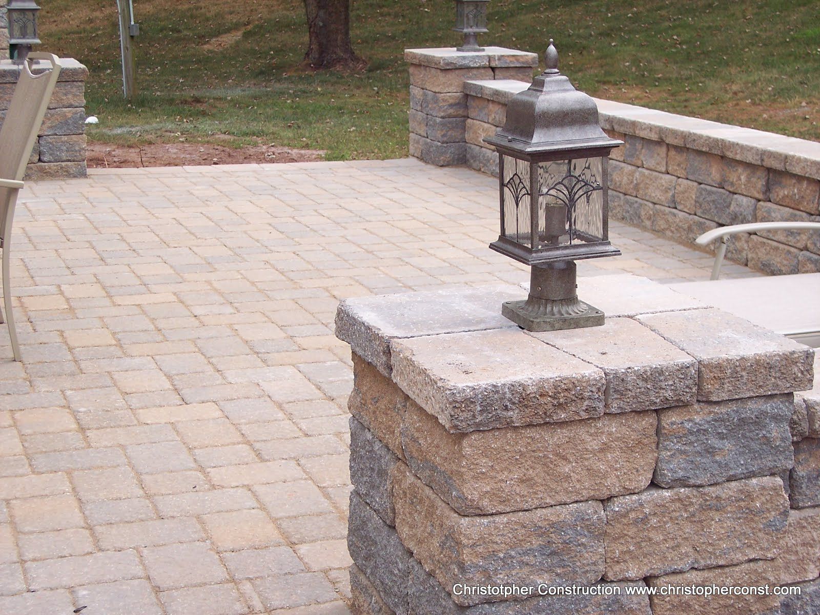 Stone patio with a decorative lantern on a low brick wall near a grassy yard