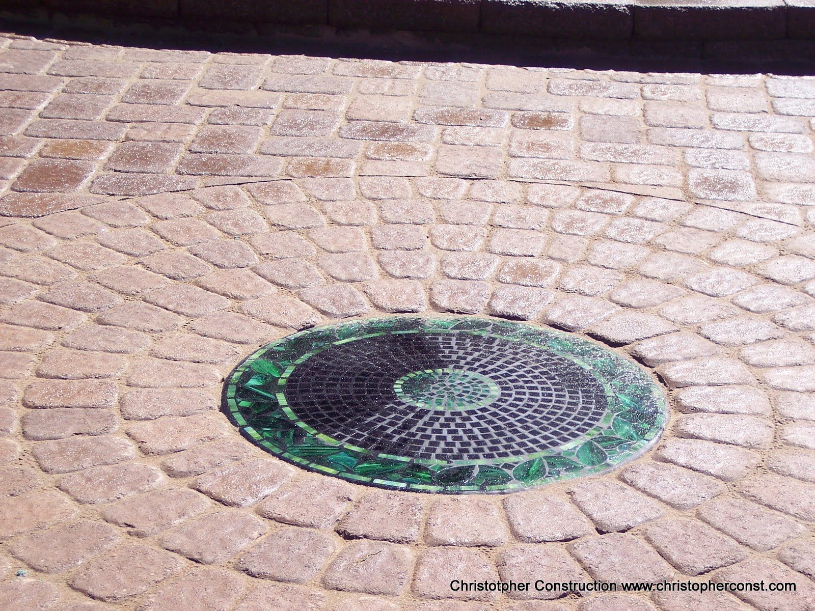 Circular manhole cover with green rim set in a brick-paved sidewalk