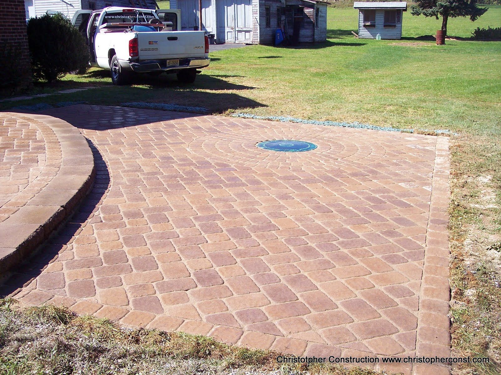 Brick driveway with a white pickup truck parked beside a grassy yard and house.