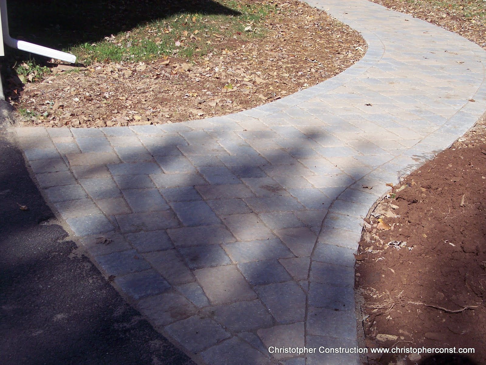Curved light-gray concrete walkway beside mulch and grass, with tree shadows across the path