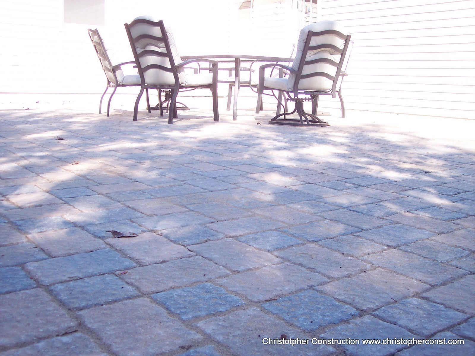 Patio table with four chairs on a sunlit stone terrace against a white wall