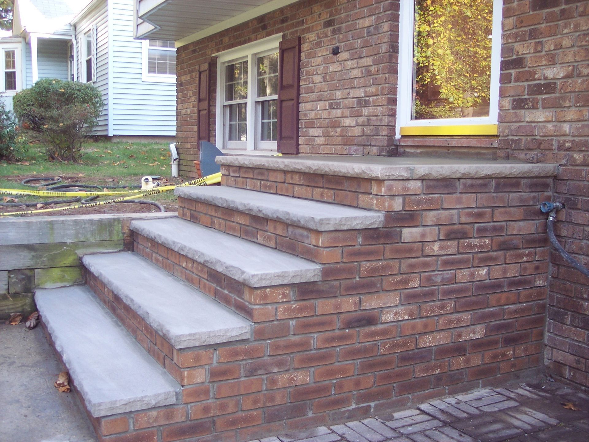 Brick house front steps with concrete treads and a small landing beside a window